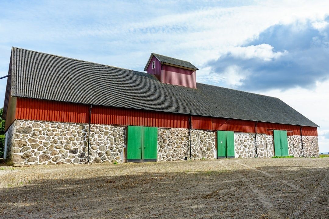Longue ferme rurale rouge en pierre, avec portes vertes